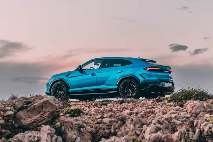 Lamborghini Urus SE: синий гибридный внедорожник на скалистом бездорожье на фоне закатного неба.