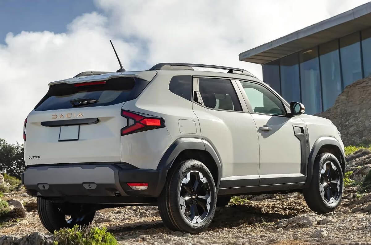 Белый Renault Duster, кроссовер, на грунтовой дороге среди камней и зелени.