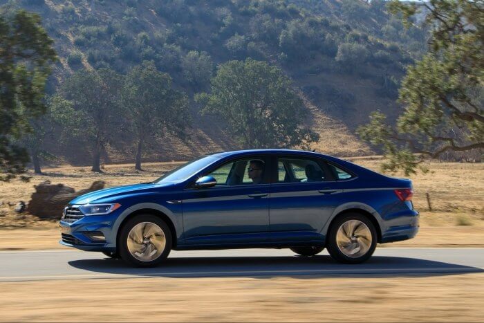 Синий Volkswagen Jetta на живописной дороге в солнечный день.